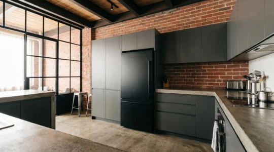 Cuisine de loft au style industriel avec murs en briques apparentes, poutrelles métalliques et réfrigérateur encastrable noir mat intégré dans la rangée de meubles