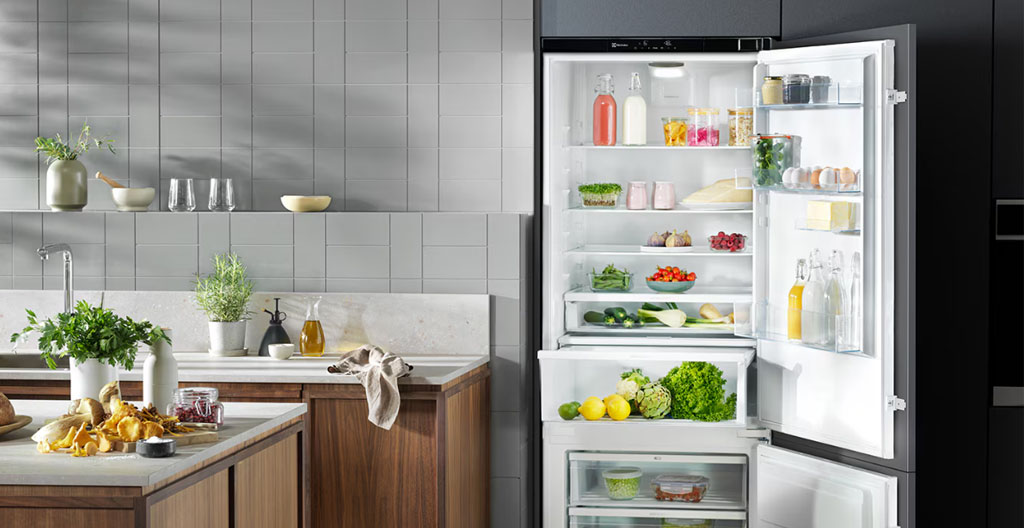 Niche dédiée encadrée par une poutre IPN métallique noire accueillant un réfrigérateur encastrable inox brossé dans une cuisine industrielle aux murs de briques apparentes